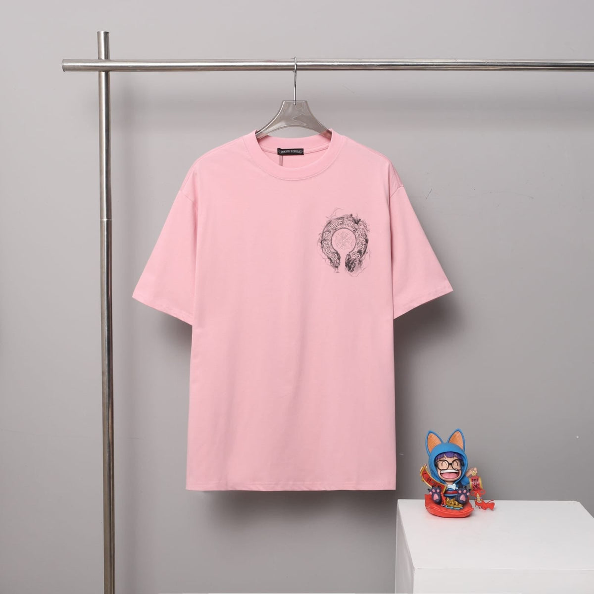 Pink t-shirt with a graphic design on a hanger against a gray background.