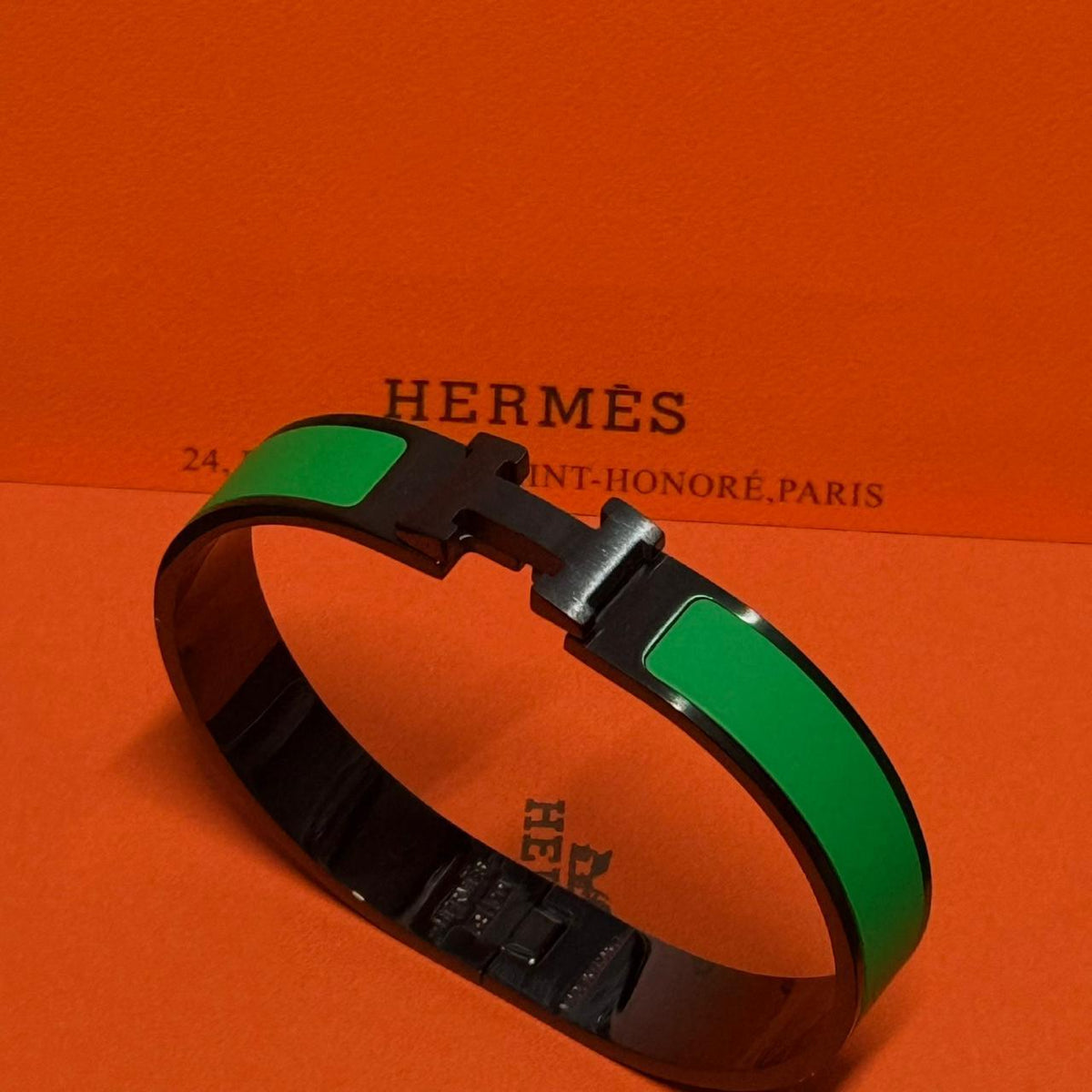 Hermes bracelet with green and black bands on an orange Hermès background