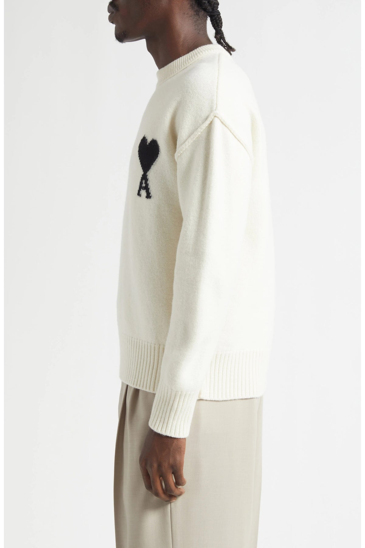 Person wearing a cream sweater with a black heart and letter 'A' design on a white background
