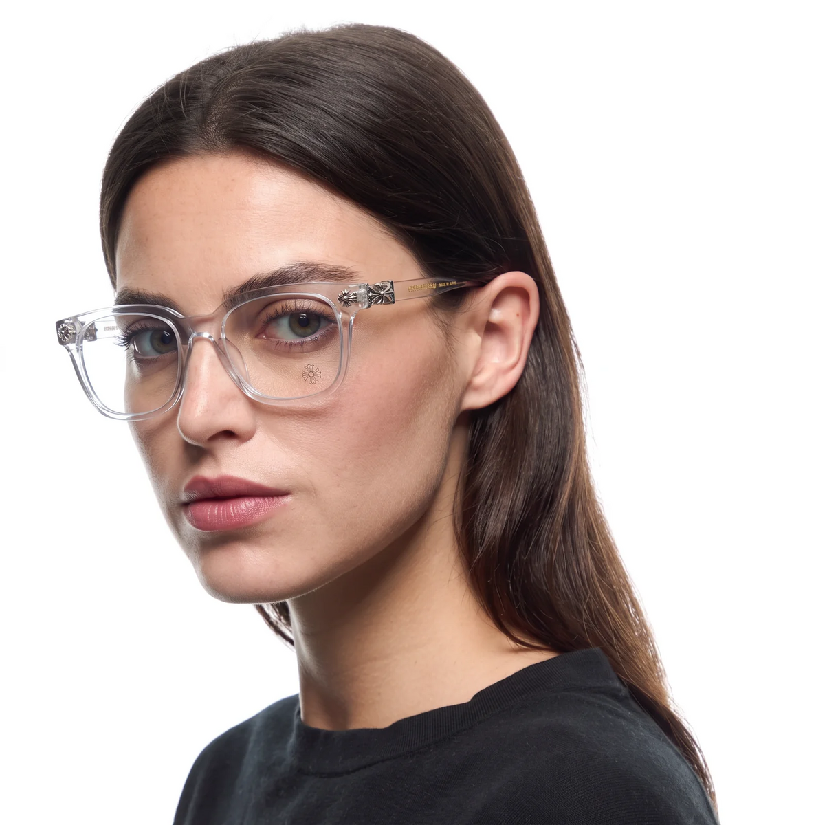 A close-up portrait of a woman wearing clear rectangular eyeglasses with a transparent frame and small decorative silver-toned details on the temples, set against a plain white background.