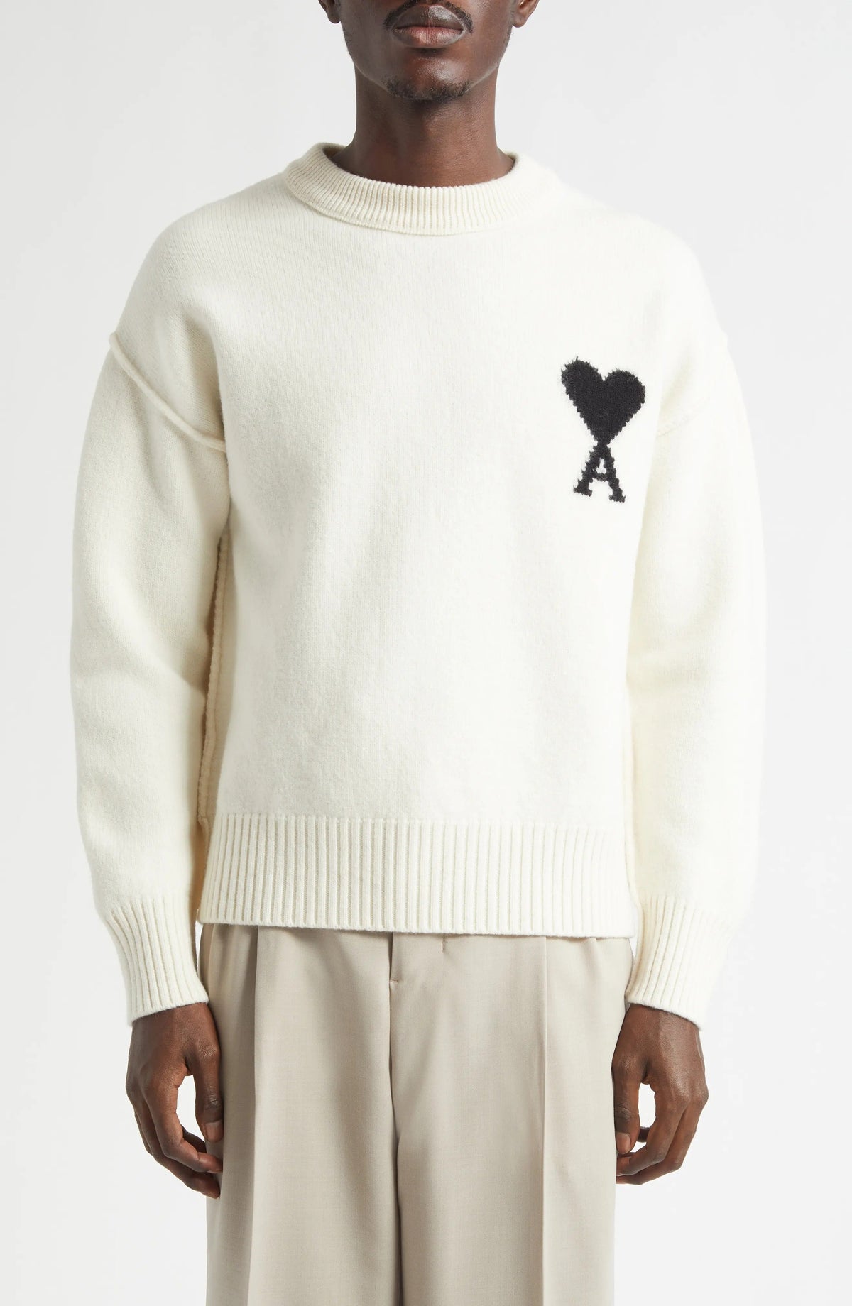 Man wearing a cream sweater with a black heart and letter 'A' design on a white background