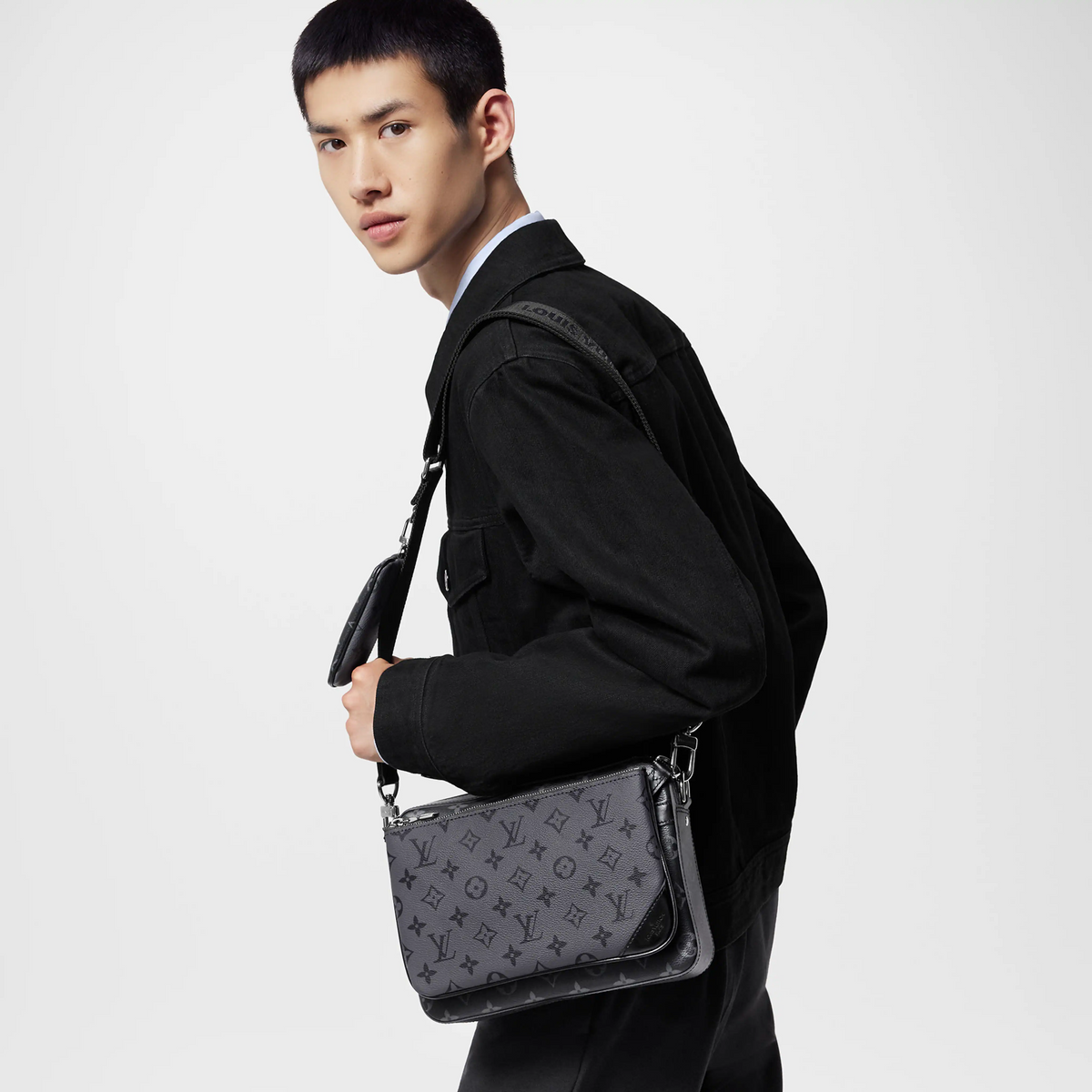 Man holding a black leather handbag with a monogram pattern on a light gray background